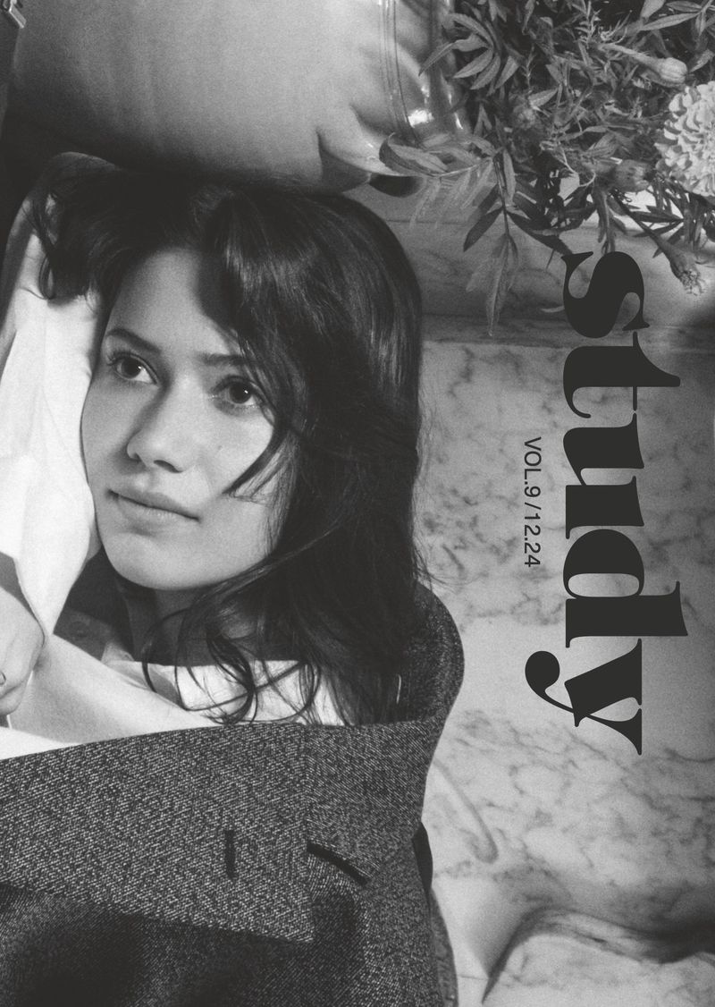 Black and white magazine cover with a young woman looking up to the side, partially draped with a patterned wool coat.