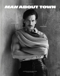 Model Jarrod Scott wearing a knit sweater and leather trousers against a textured wall for Man About Town.