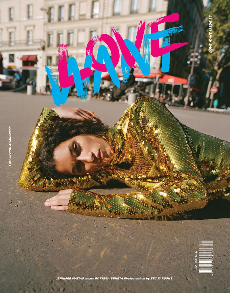 Magazine cover featuring a woman in a gold sequin dress lying on a city street in Paris, with building facades and colorful lettering.