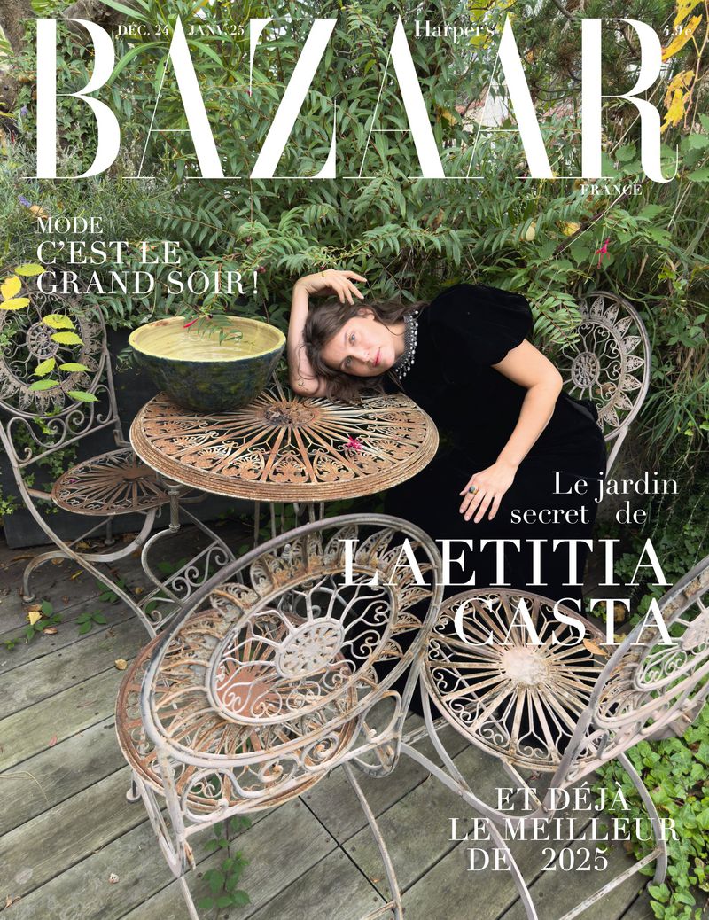 Fashion magazine cover featuring Laetitia Casta in black dress, reclining on metal garden furniture, surrounded by lush greenery, Harper's Bazaar.