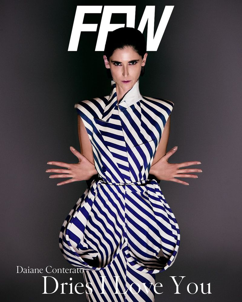 Editorial fashion portrait of a woman with dark hair wearing a striped dress, posing against a dark grey background in a studio setting.