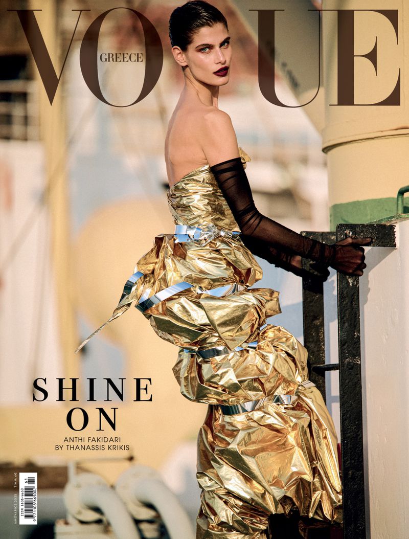 Vogue Greece cover featuring a posed fashion model wearing a gold textured gown, sheer black gloves, and dark lipstick, standing outdoors.