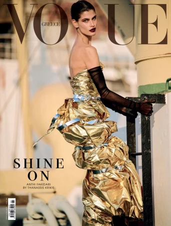 Vogue Greece cover featuring a posed fashion model wearing a gold textured gown, sheer black gloves, and dark lipstick, standing outdoors.