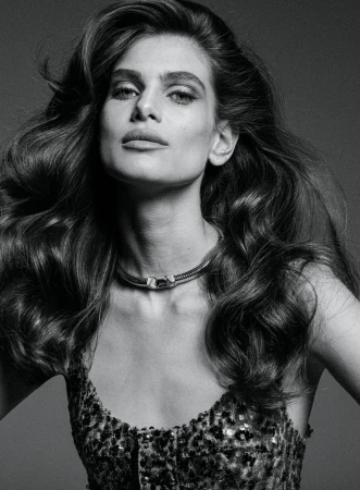 Monochrome close-up portrait of an adult woman with long wavy hair, a choker necklace, and a sequined top against a grey background.