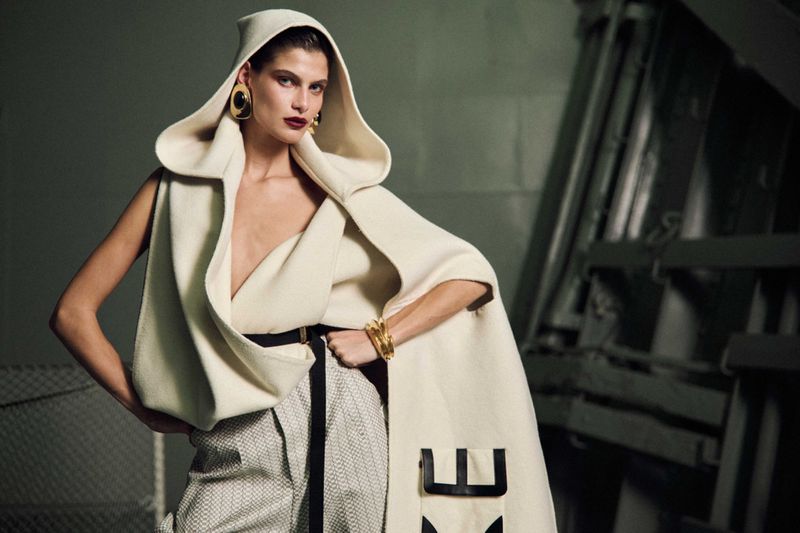 Model Anthi Fakidari wearing a hooded cream wool cape and patterned trousers for Vogue Greece