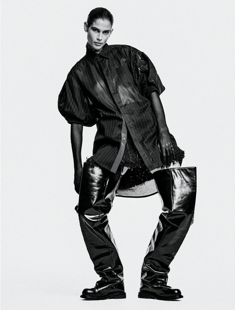 Monochrome fashion shot of an adult female model in a short, shimmering dress, oversized striped shirt, and shiny black thigh-high boots.