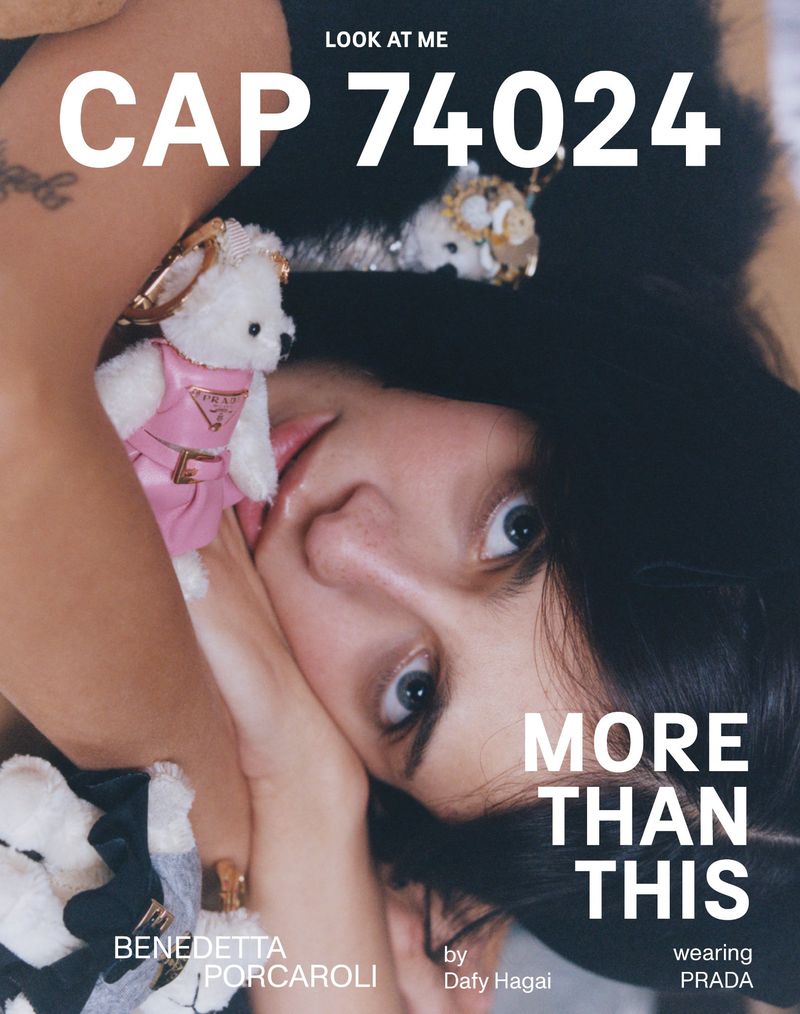 Close-up fashion editorial featuring a young female model with dark hair, lying down wearing a black top with teddy bear accessories.
