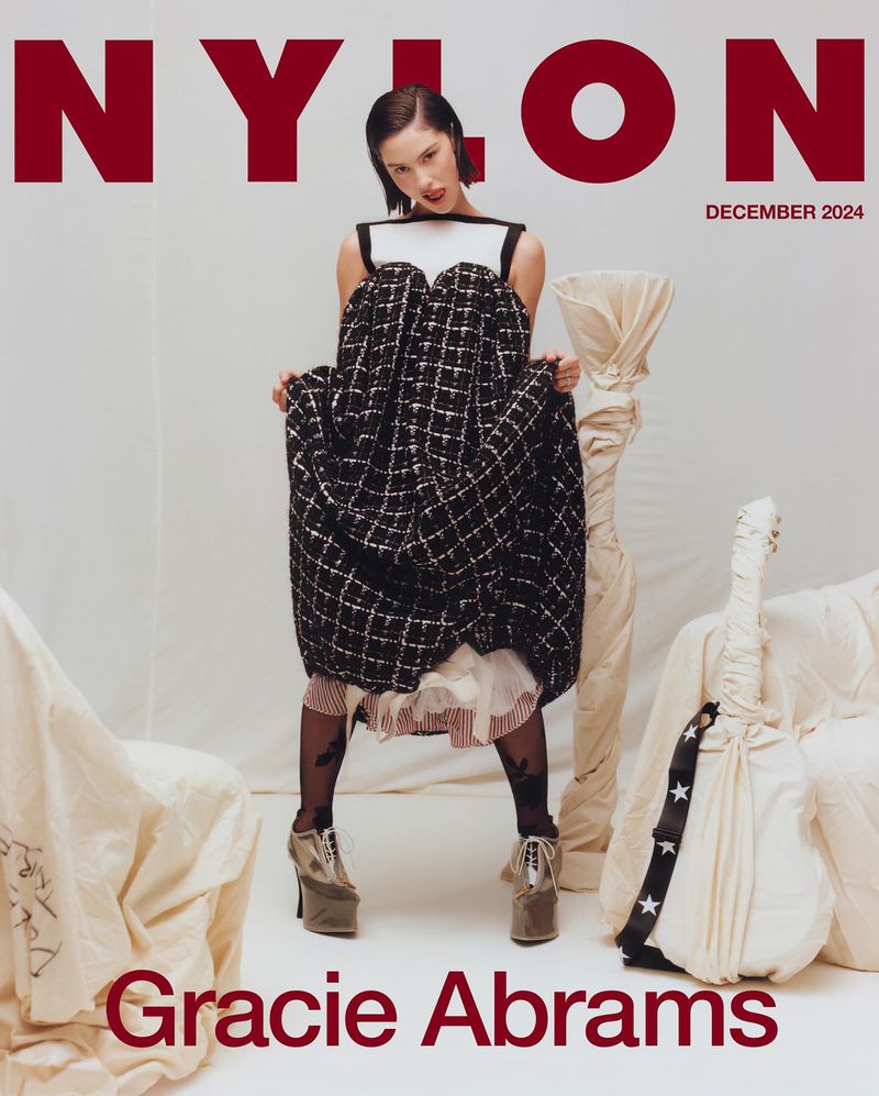 Gracie Abrams on NYLON cover, December 2024 issue. She wears a unique dress and platform shoes, in a photo studio setting with props.