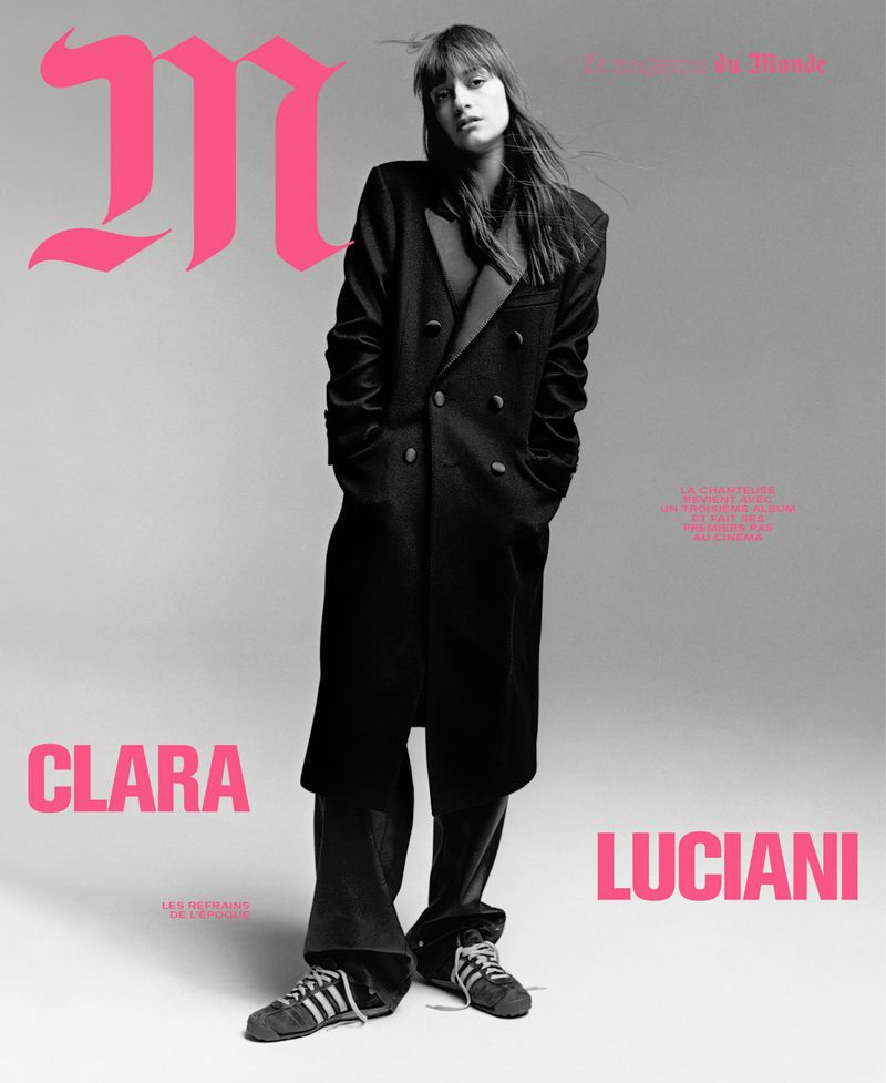 Black and white magazine cover featuring a woman in a black coat, standing in front of pink text, creating a striking contrast.