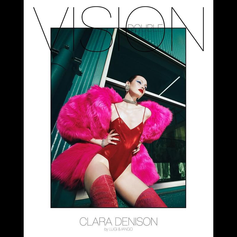 Fashion model in a red bodysuit and bright pink fur coat poses against a green backdrop with a sleek modern window design.