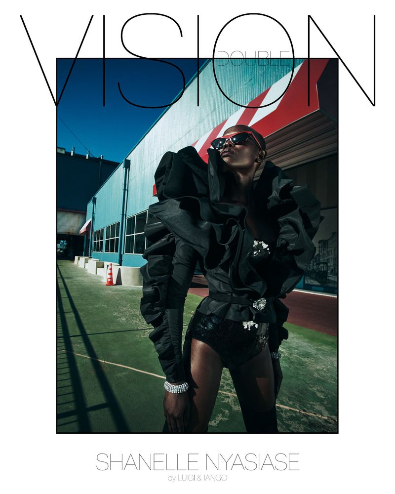 Fashion photo of a Black female model wearing sunglasses and an avant-garde black outfit with large ruffles posing on an outdoor sports court.