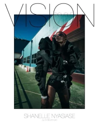 Model in black ruffled top and shorts standing outdoors in front of a blue building under a clear blue sky for Double Vision holiday cover.