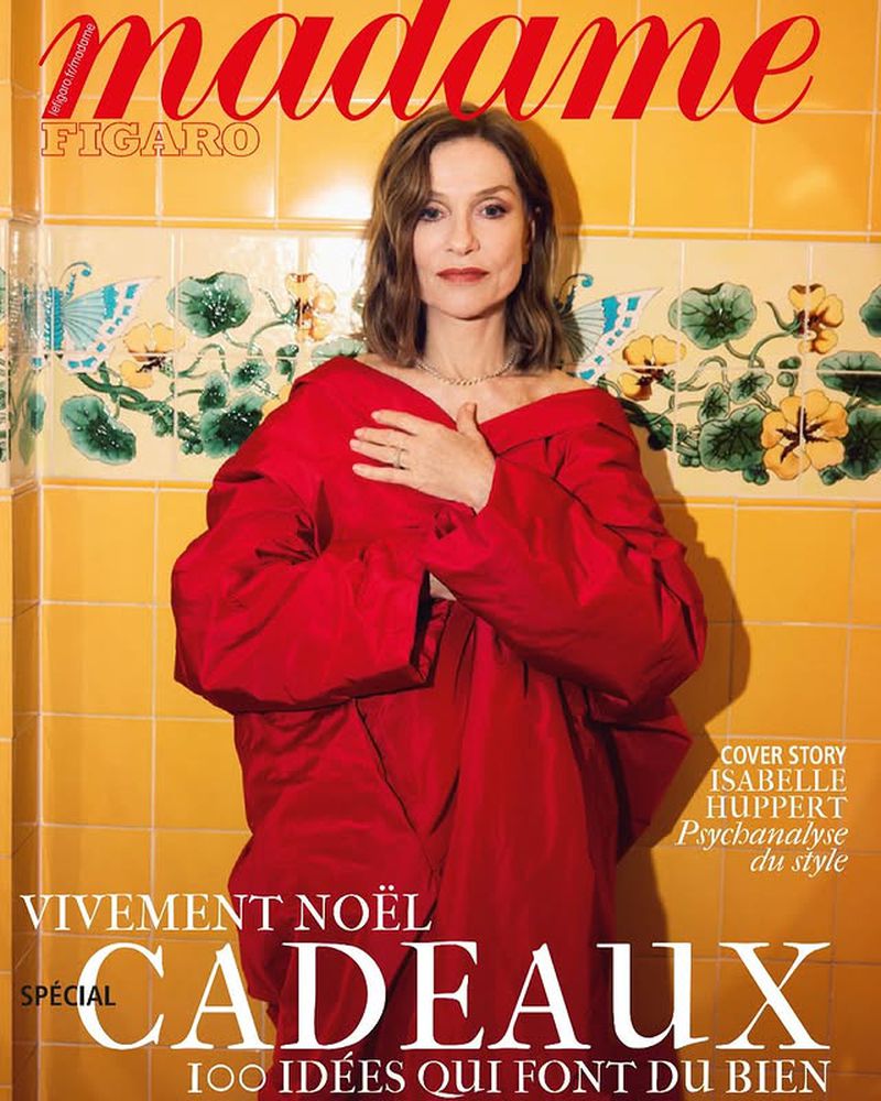 Magazine cover of Madame Figaro featuring Isabelle Huppert in a red outfit against a yellow tiled wall with floral details.