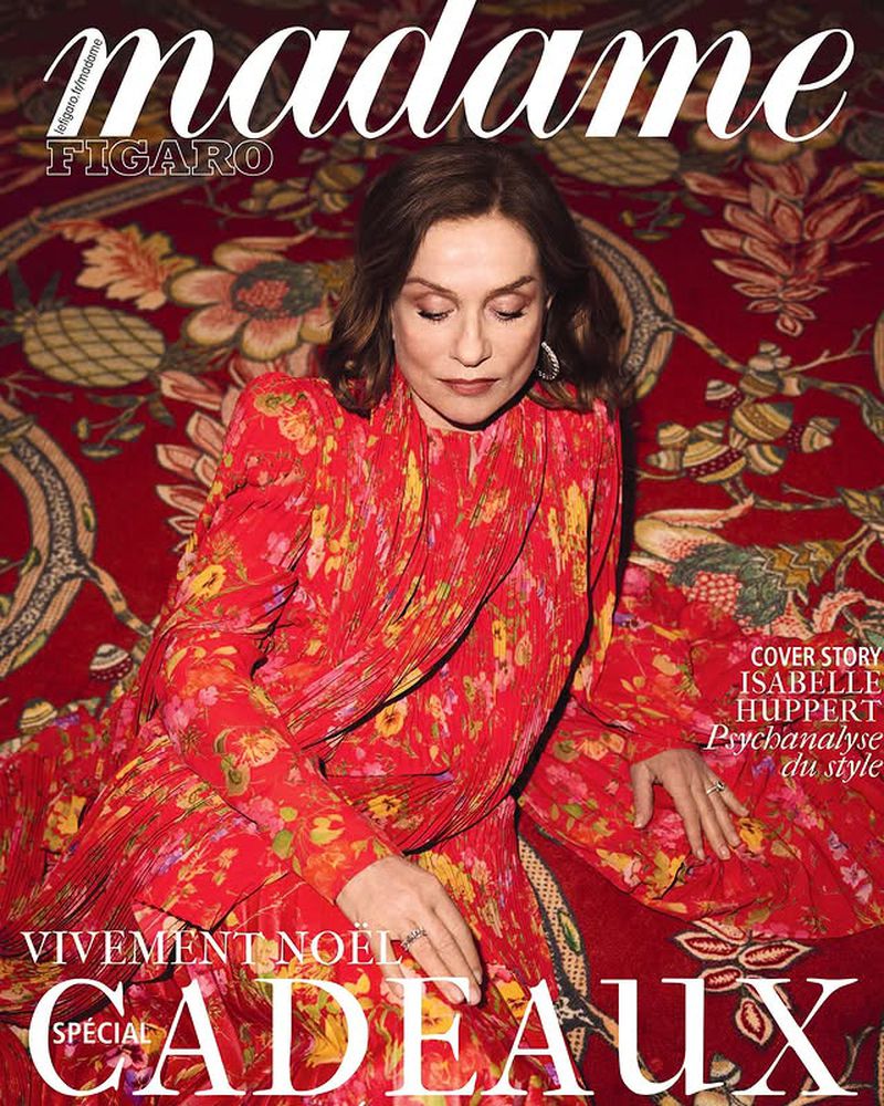 Magazine cover featuring a portrait of actress Isabelle Huppert in a red floral dress against a patterned background, showcasing fashion and editorial style.
