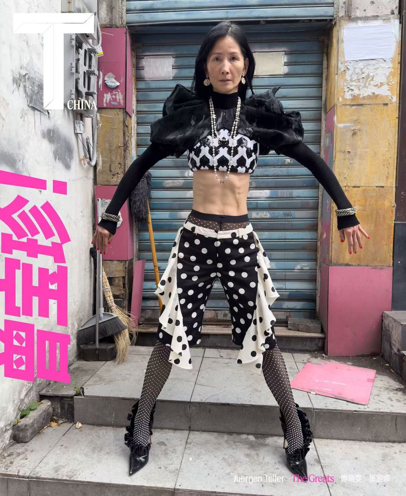 Editorial fashion shot of a woman with a black and white outfit posing in an alleyway with a broom and metal garage door in the background.