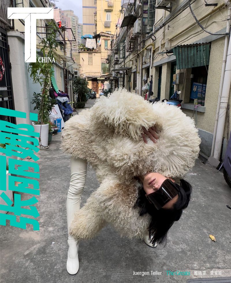 Editorial shot of a woman in a large, furry coat, white pants, and boots bending over backwards in an alleyway, fashion photoshoot.