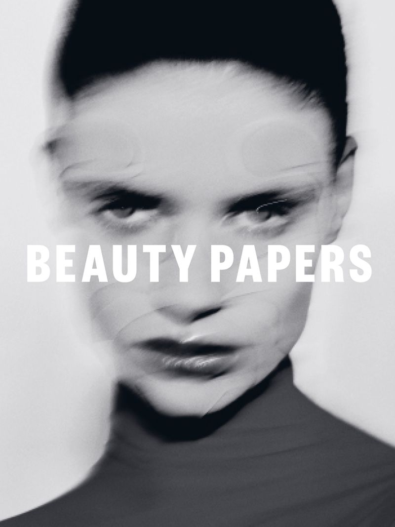 Monochrome portrait of an adult woman with soft focus and blurred effect, wearing a high-neck top, featuring the text 'Beauty Papers'.