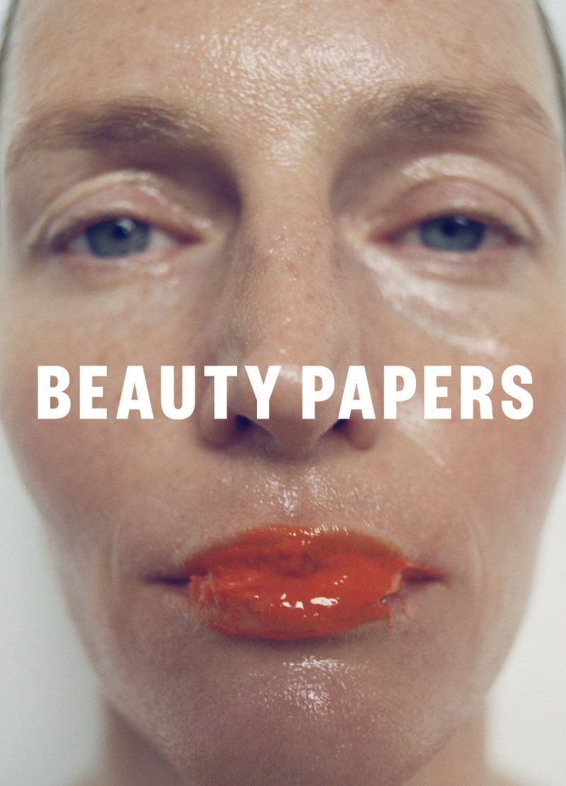 Close-up of a woman's face with a glossy finish and vibrant red lips, highlighting beauty and skincare with a stark white background.