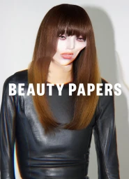Model with long brown hair and bangs wearing a black top against a plain white background for Beauty Papers Issue 12