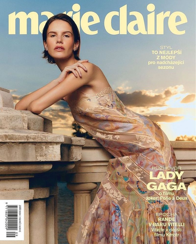 Magazine cover featuring a female model in a floral dress, posing on a stone balcony with a sky background, showcasing fashion and style.