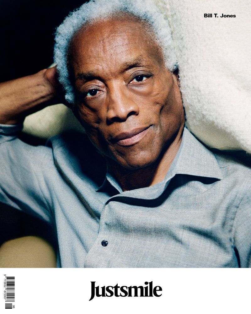 Portrait of an African American man with short gray hair, wearing a gray button-down shirt and reclining against a light-colored cushion.