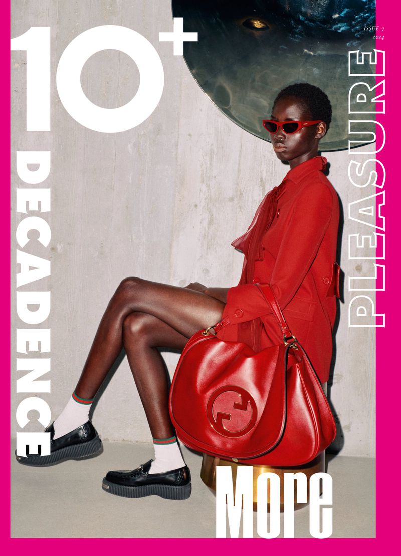 Model in a red jacket and red sunglasses sitting with a large red leather handbag and black loafers on a magazine cover.