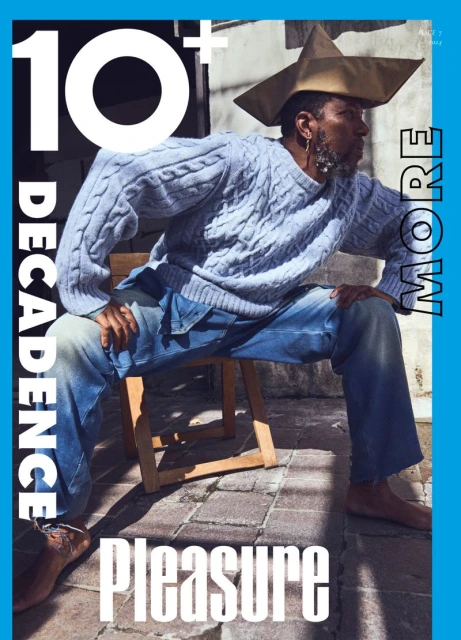 Magazine cover featuring a stylish adult male in a paper hat and cable-knit sweater, seated outdoors against a neutral backdrop, with bold text.
