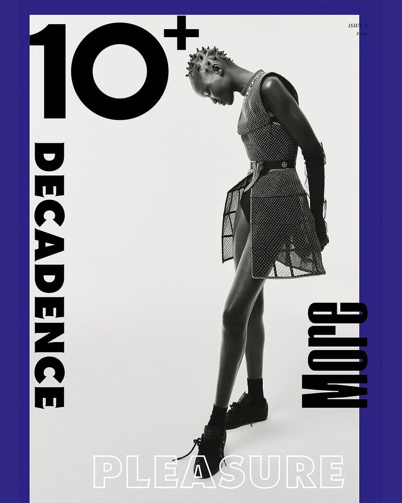 Black female model poses in a translucent black mesh dress with black boots against a white background in a fashion editorial shot.