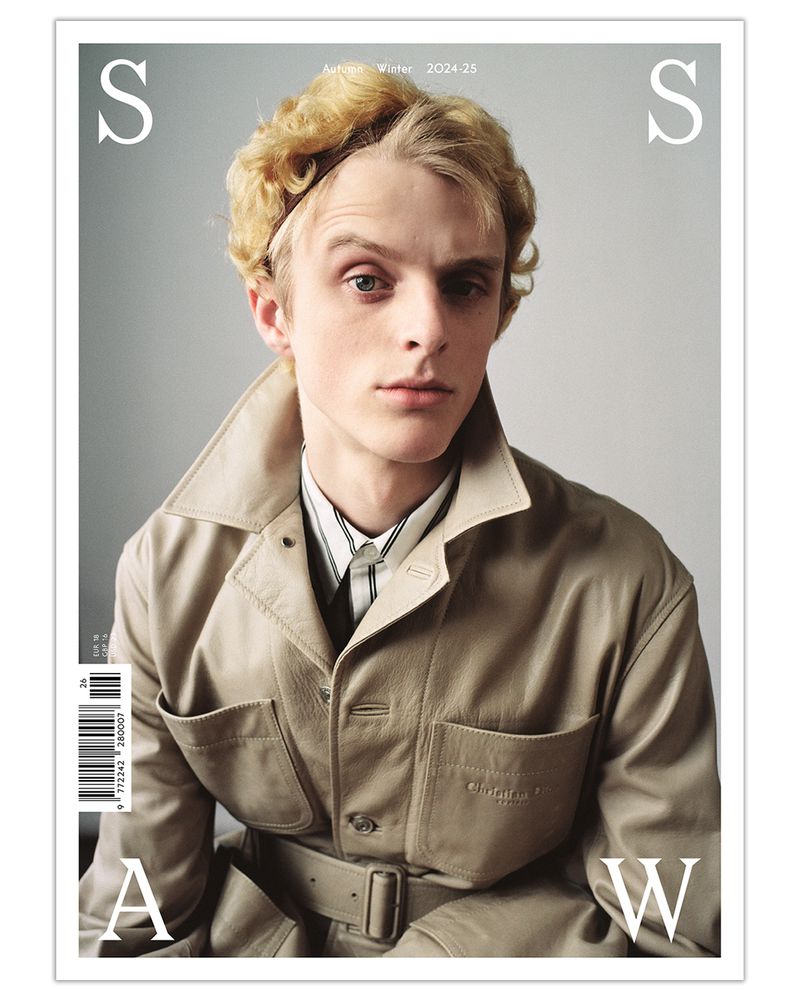 Magazine cover featuring a blonde male model in a tan trench coat against a grey background. Autumn Winter 2024-25 fashion.