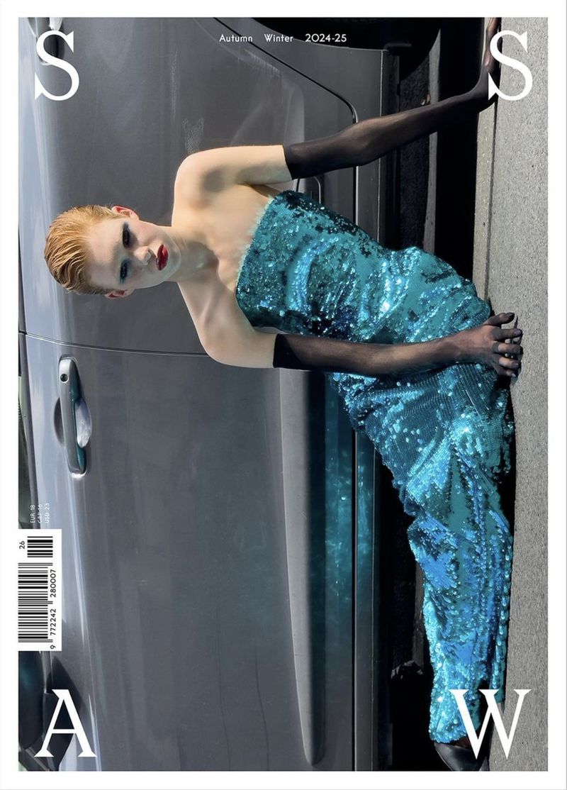 Fashion editorial featuring a model in a sequined blue gown posing next to a grey vehicle. Autumn Winter 2024-25 text is present.