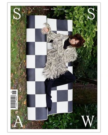 Magazine cover featuring a woman in a shaggy jacket reclining on a black and white checkered surface in a lush, green outdoor setting.