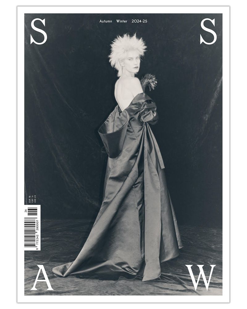 Fashion magazine cover featuring a woman in a dramatic gown, posing against a draped background with a monochrome color palette.