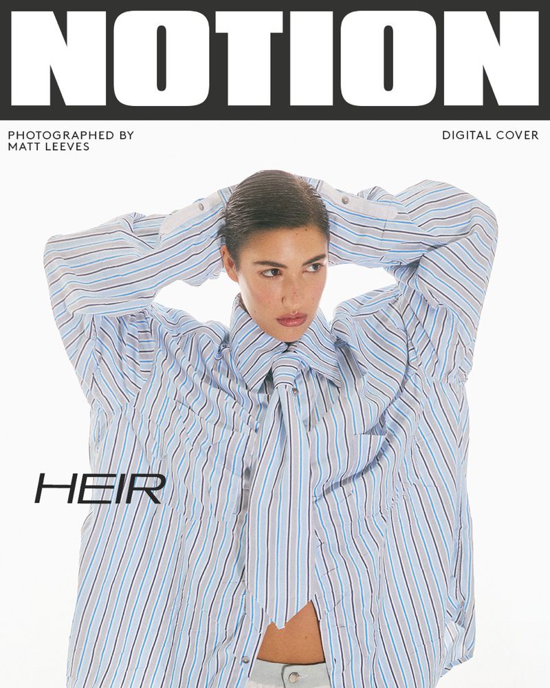 Magazine cover featuring a woman in an oversized blue and white striped shirt, gazing off-camera with a white background and bold text.
