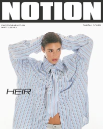 Model with slicked-back hair wearing an oversized blue striped shirt with hands behind head against a white background