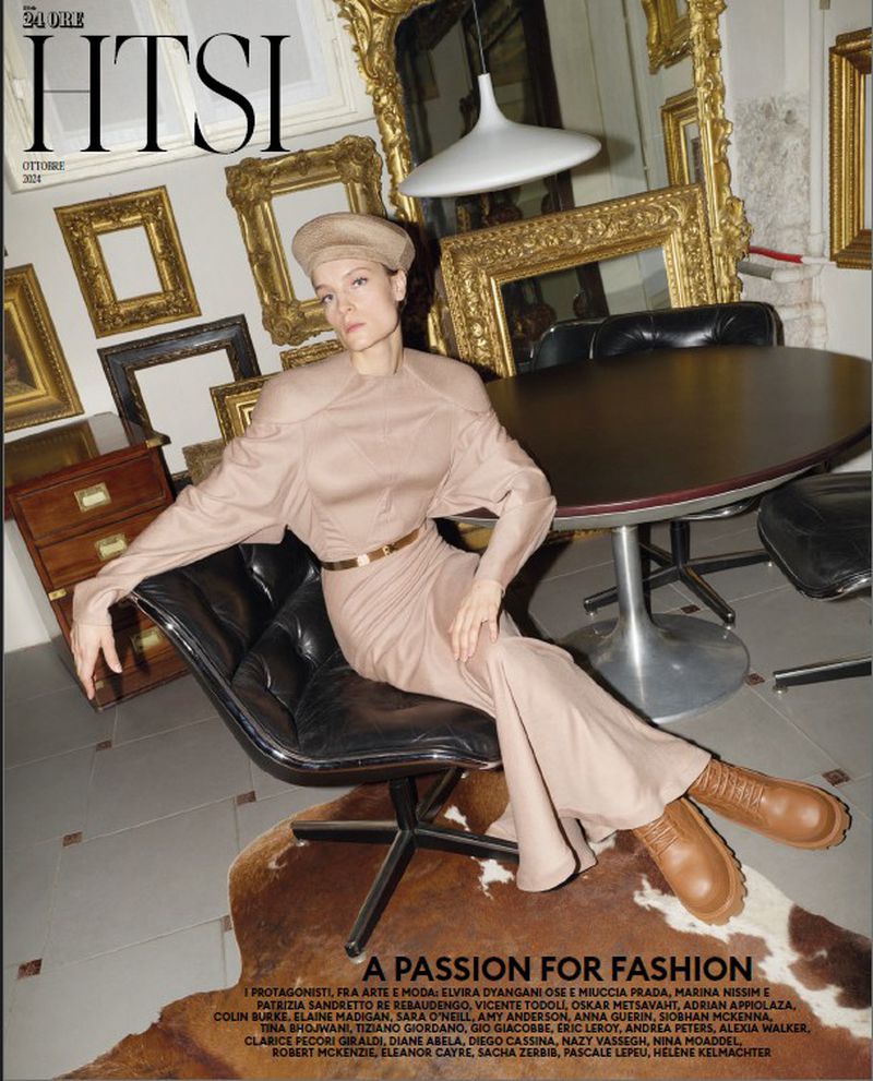Fashion magazine cover featuring a woman in a light brown dress and boots, posing in a chair surrounded by antique frames.