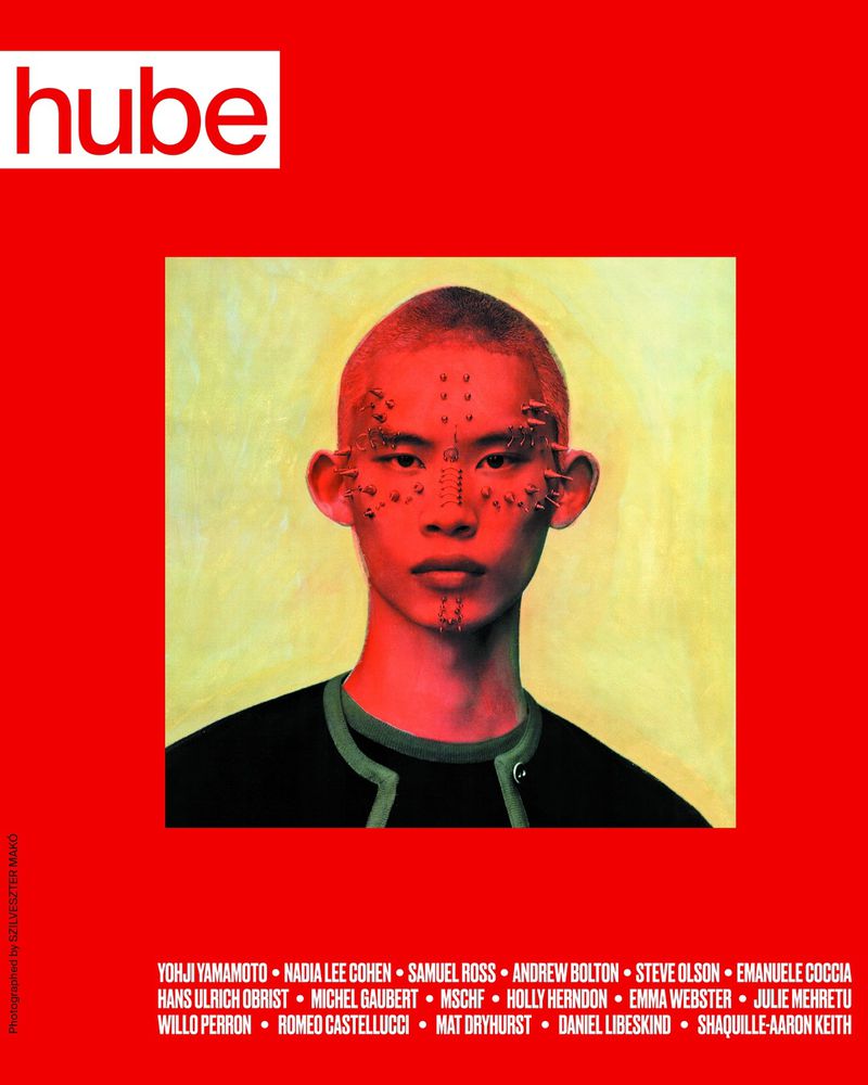 Magazine cover with a portrait of a person with facial piercings against a red backdrop. Features the 'hube' logo and a list of names.
