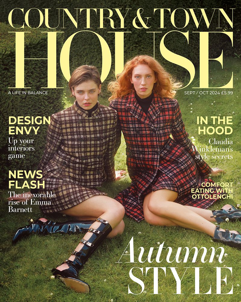 Two women wearing plaid outfits pose for the cover of Country & Town House magazine on green grass outdoors in natural light.