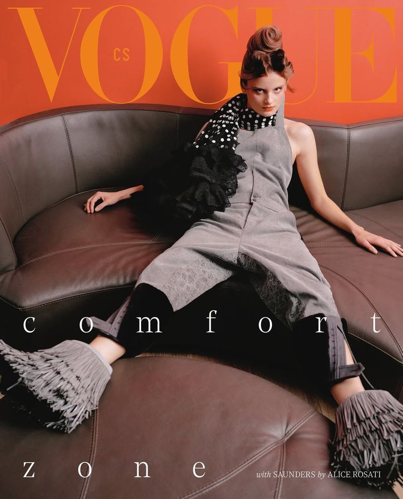 Vogue magazine cover featuring a woman in grey jumpsuit and polka dot scarf reclining on a brown leather couch.