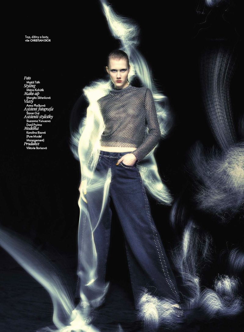 Fashion editorial shot of a female model in a mesh top and wide-leg jeans, posed in a studio with light painting effects.