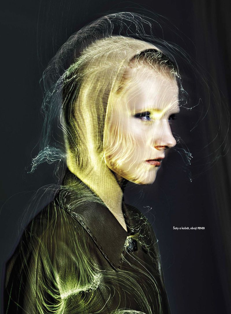 Abstract beauty shot of a model with ethereal light effect, wearing a dark jacket, set against a dark background in a photo studio.