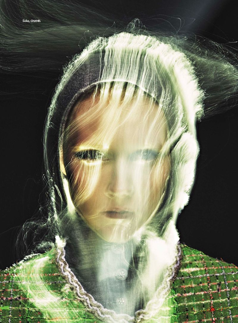 Close-up portrait of a young woman with long exposure light effects on her face, wearing a patterned green tweed jacket against a black backdrop.