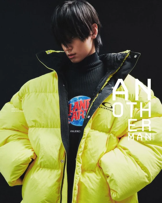 Young man wearing a bright yellow puffer jacket and black turtleneck against a dark studio background
