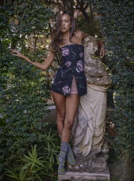 Model leaning against a stone statue surrounded by lush green foliage for a Remix Magazine editorial by Steven Chee