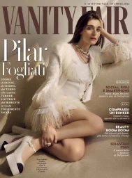 Pilar Fogliati seated on a sofa wearing a feathered white jacket and platform heels for Vanity Fair Italia