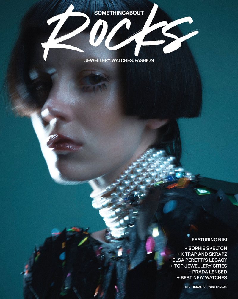 Fashion magazine cover featuring a model wearing statement jewelry, shot in a studio setting with a teal background.