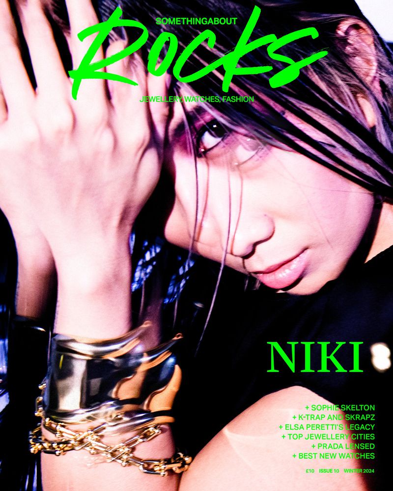 Magazine cover featuring a woman with dark hair, close-up shot, adorned with gold bracelets, against a dark background.