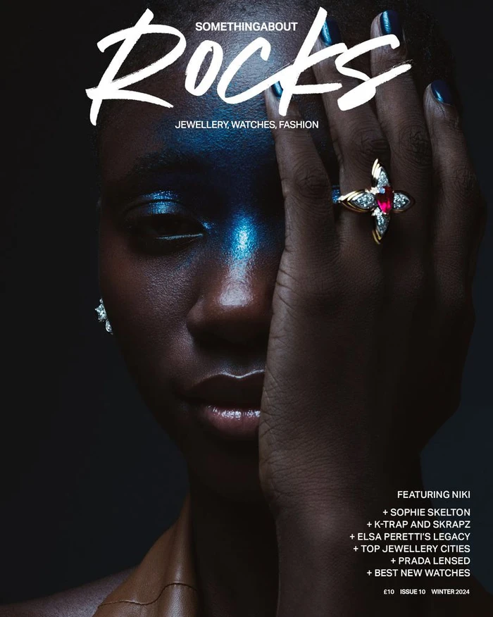 Close-up portrait of a Black woman covering half her face with her hand, wearing an ornate gold ruby ring for a magazine cover.
