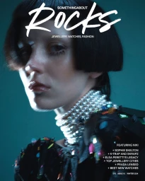 Close-up portrait of a woman wearing a heavy layered pearl choker and dark outfit against a teal background.