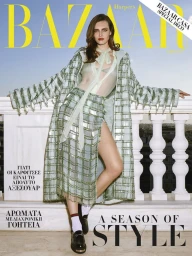 Model leaning against a white balustrade wearing a patterned green coat, matching skirt, white socks, and loafers against an open sky.
