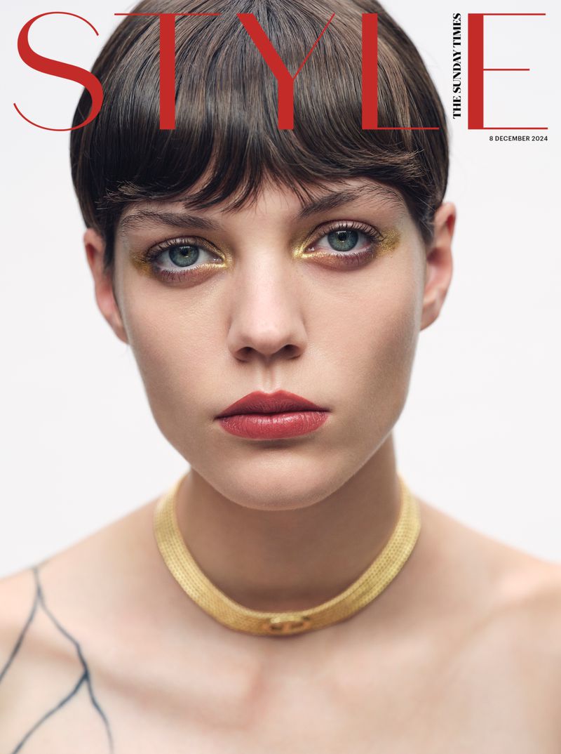 Fashion magazine cover featuring a close-up portrait of a model with short dark hair, gold eye makeup, and a gold choker necklace.